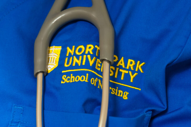 A stethoscope hangs over North Park university school of nursing logo on blue scrubs.