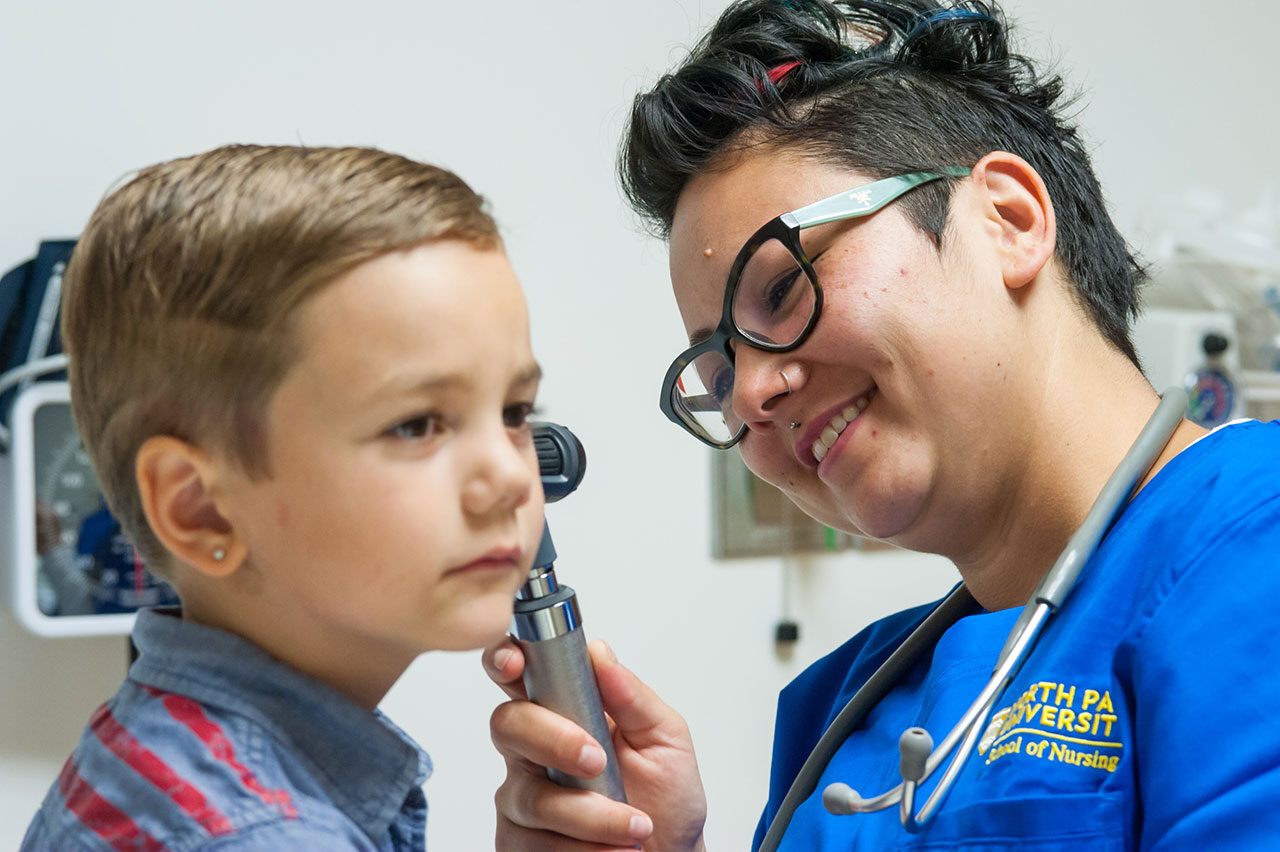 A student nurse uses an otoscope to inspect a child's ear.