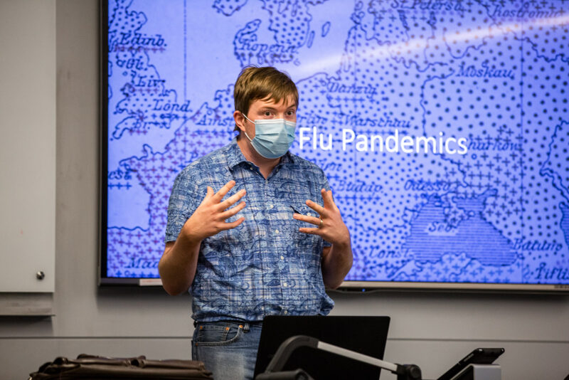 Professor wearing cloth face mask lectures with powerpoint slide showing map of 