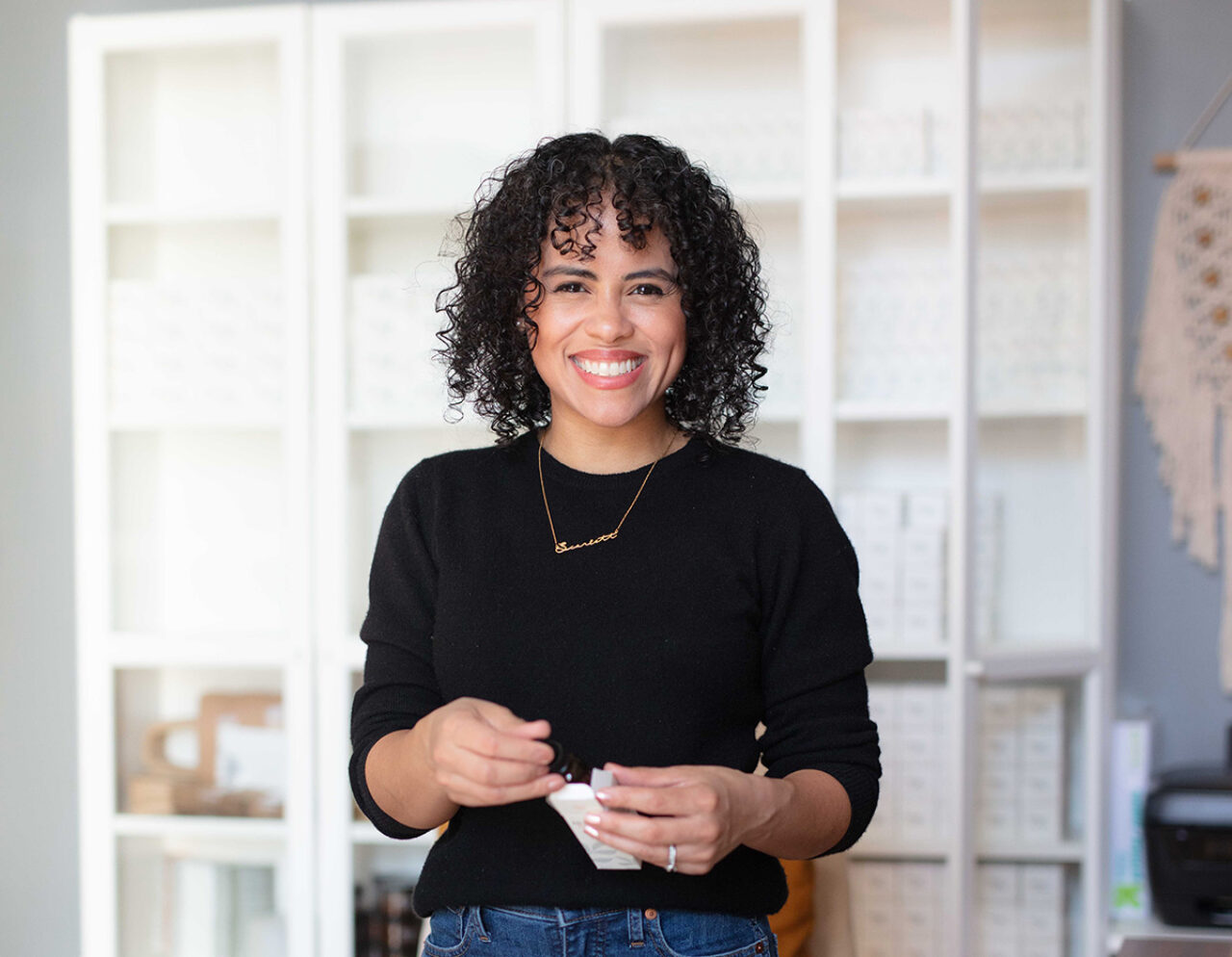 Woman stands in sunlit workspace holding a bottle of essential oil.