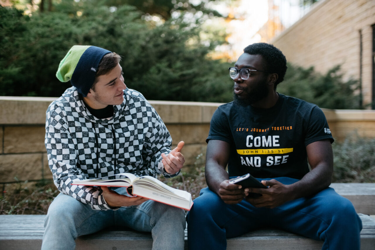 Two students sitting on a bench talking.