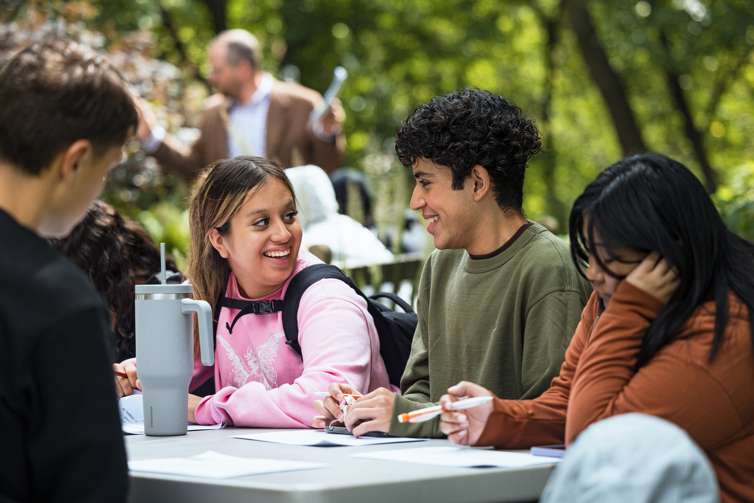 Two students sitting at a table filling out paperwork and smiling at each other.