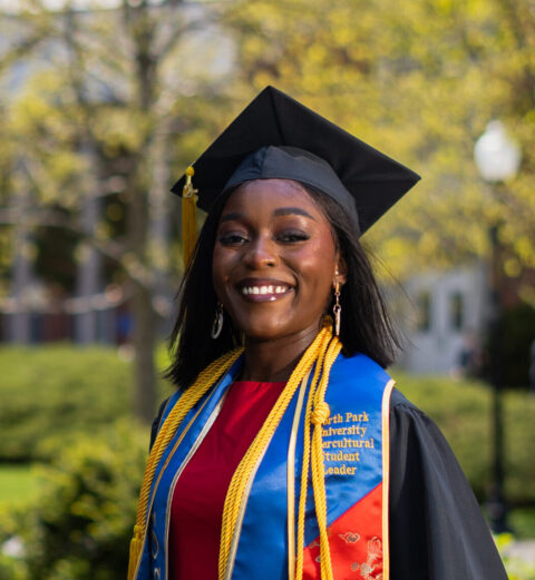 a young woman standing outdoors in graduation cap and gown.