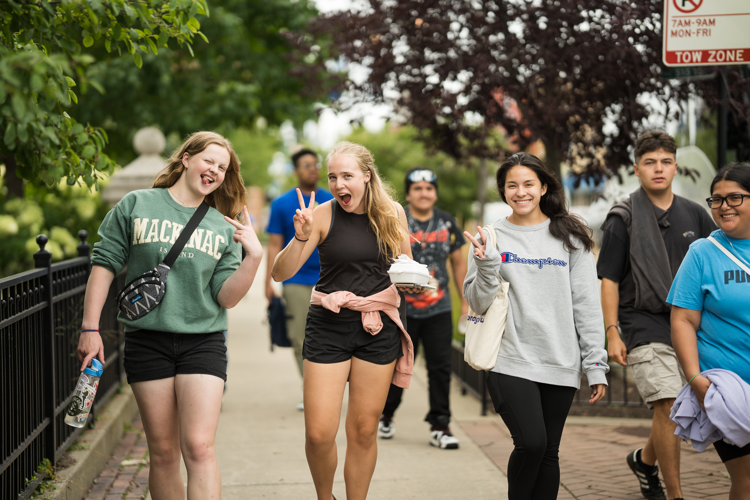 Students smiling and walking down the sidewalk next to North Park's campus in the summer.