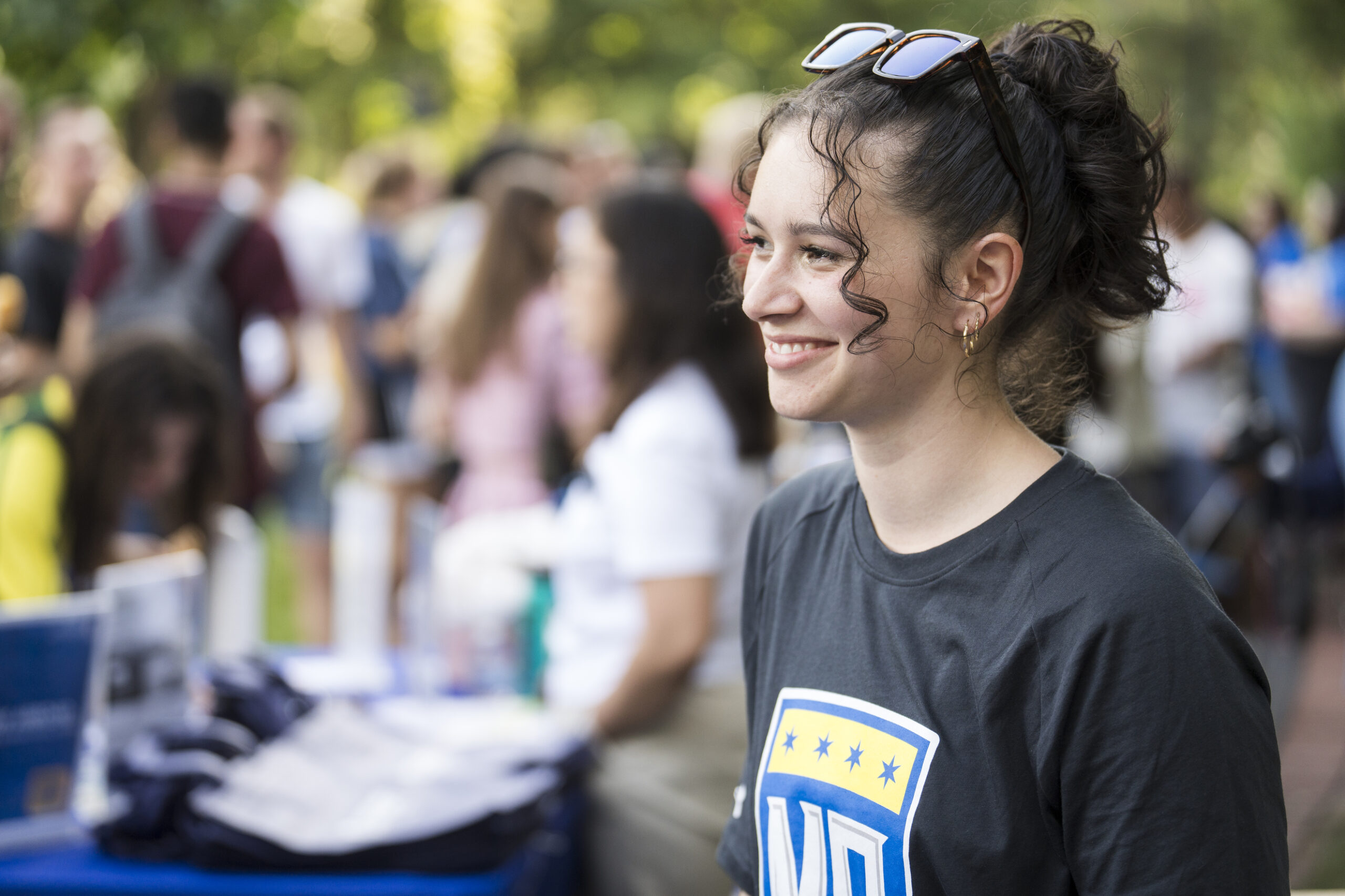 A student smiling and wearing a North Park athletics shirt at a busy visit event outdoors.
