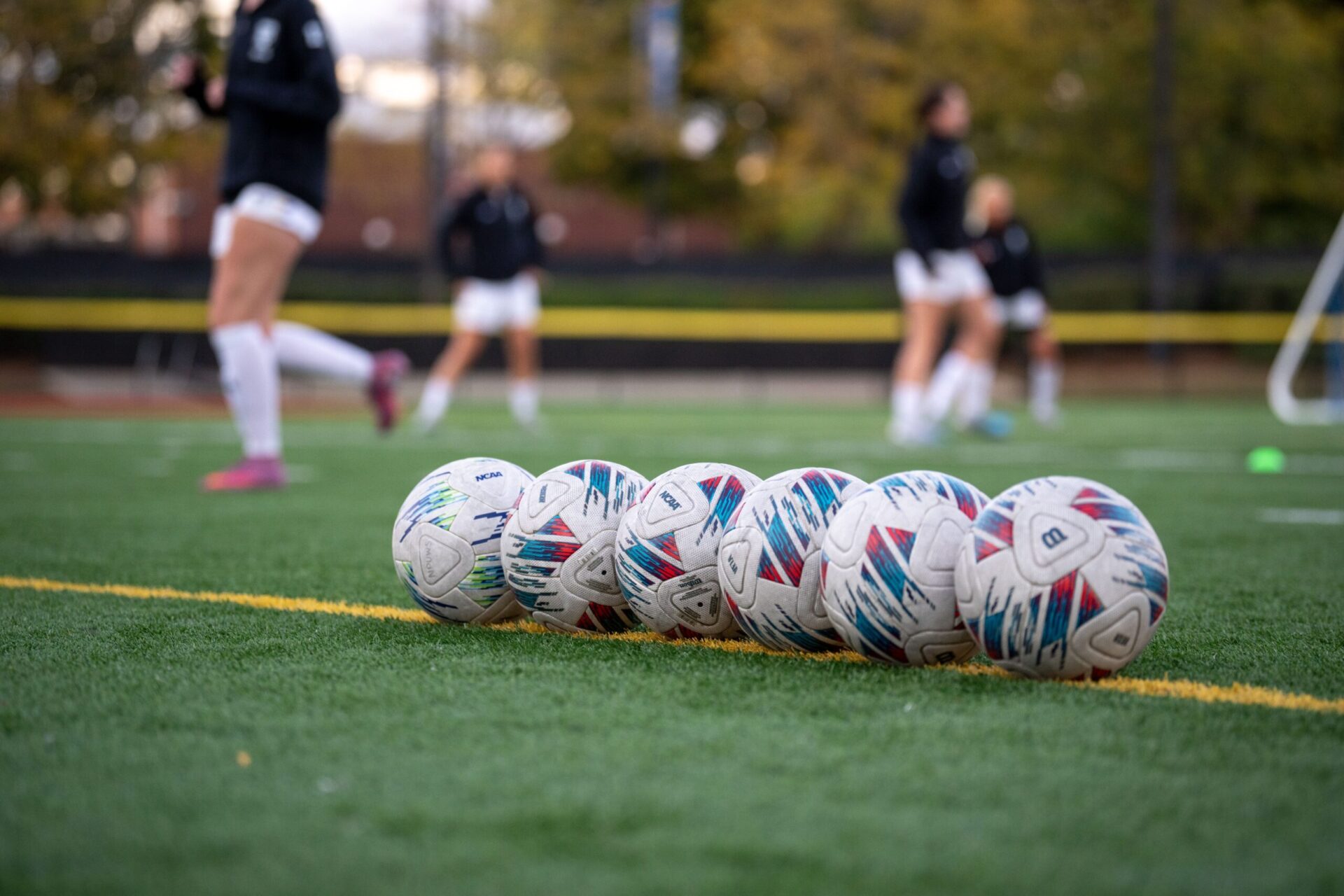 Six soccer balls lined up on a field during the team's warmups.