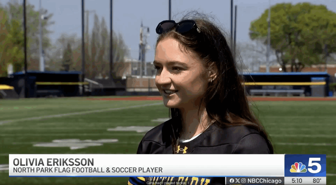 North Park University student-athlete Olivia Eriksson talks to an NBC Chicago reporter about her experience on the university's flag football team while wearing her jersey. She is standing on the school's football field.