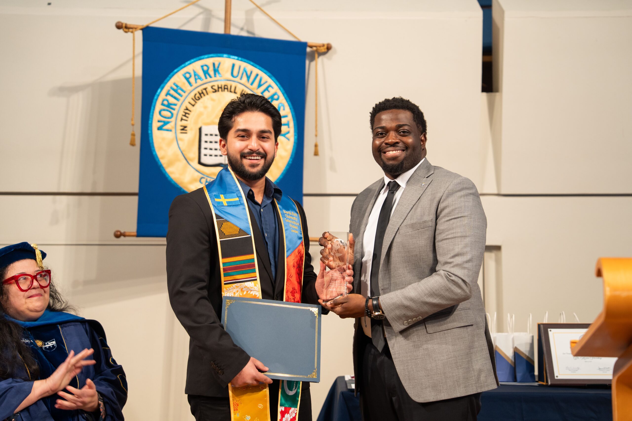 A student accepts an award from a North Park University staff member. The student has on a colorful stole.