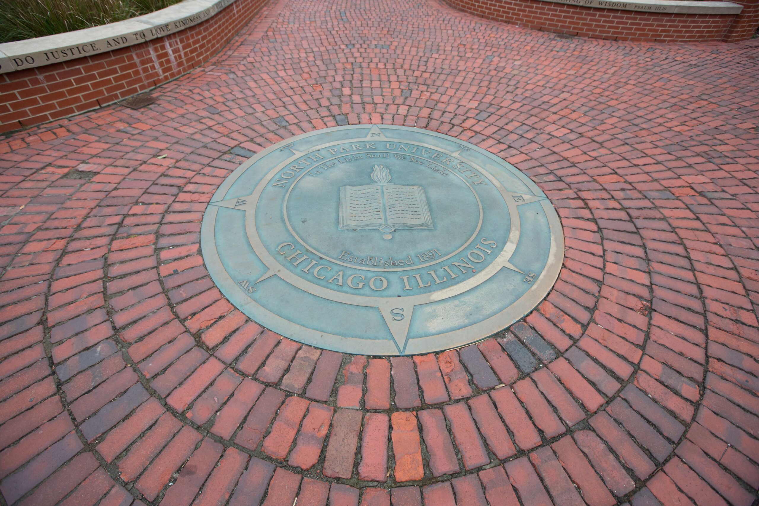 The North Park University seal, a compass, on the ground with brick red brick laid around it.
