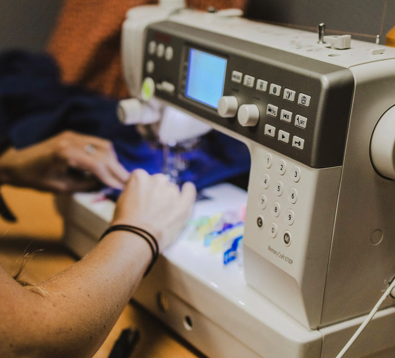 A close-up of a sewing machine in which you can see an individual's hands sewing a piece of fabric.