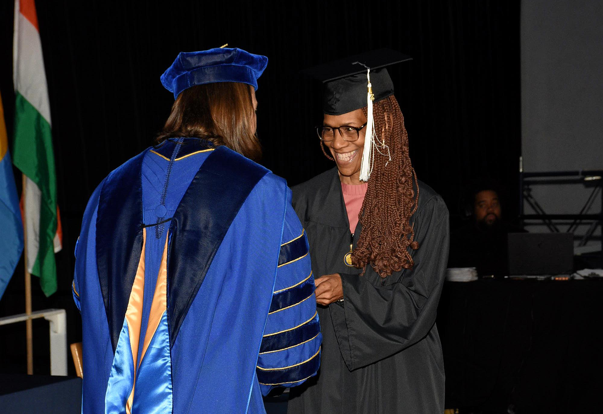 At a Commencement service, a woman in graduation regalia shakes hands with the president of North Park University while receiving her diploma.
