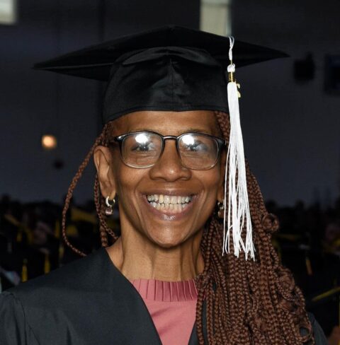 A woman smiles with a graduation cap and gown on.