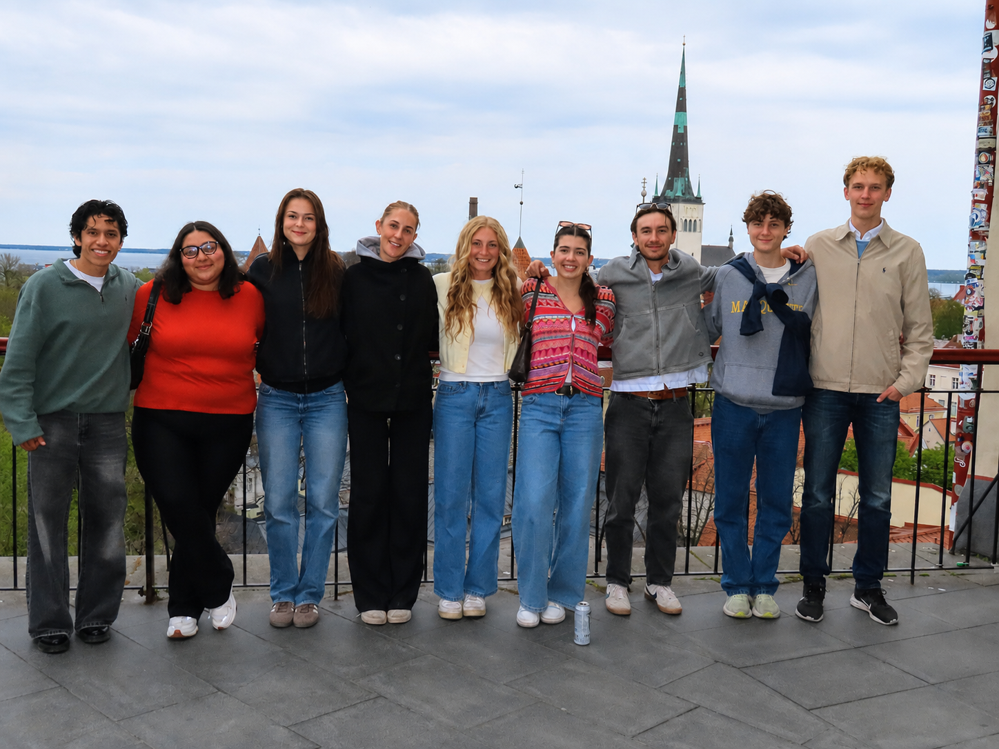 A group of students stand with their arms around each other. They are in a city in Estonia with the skyline behind them.