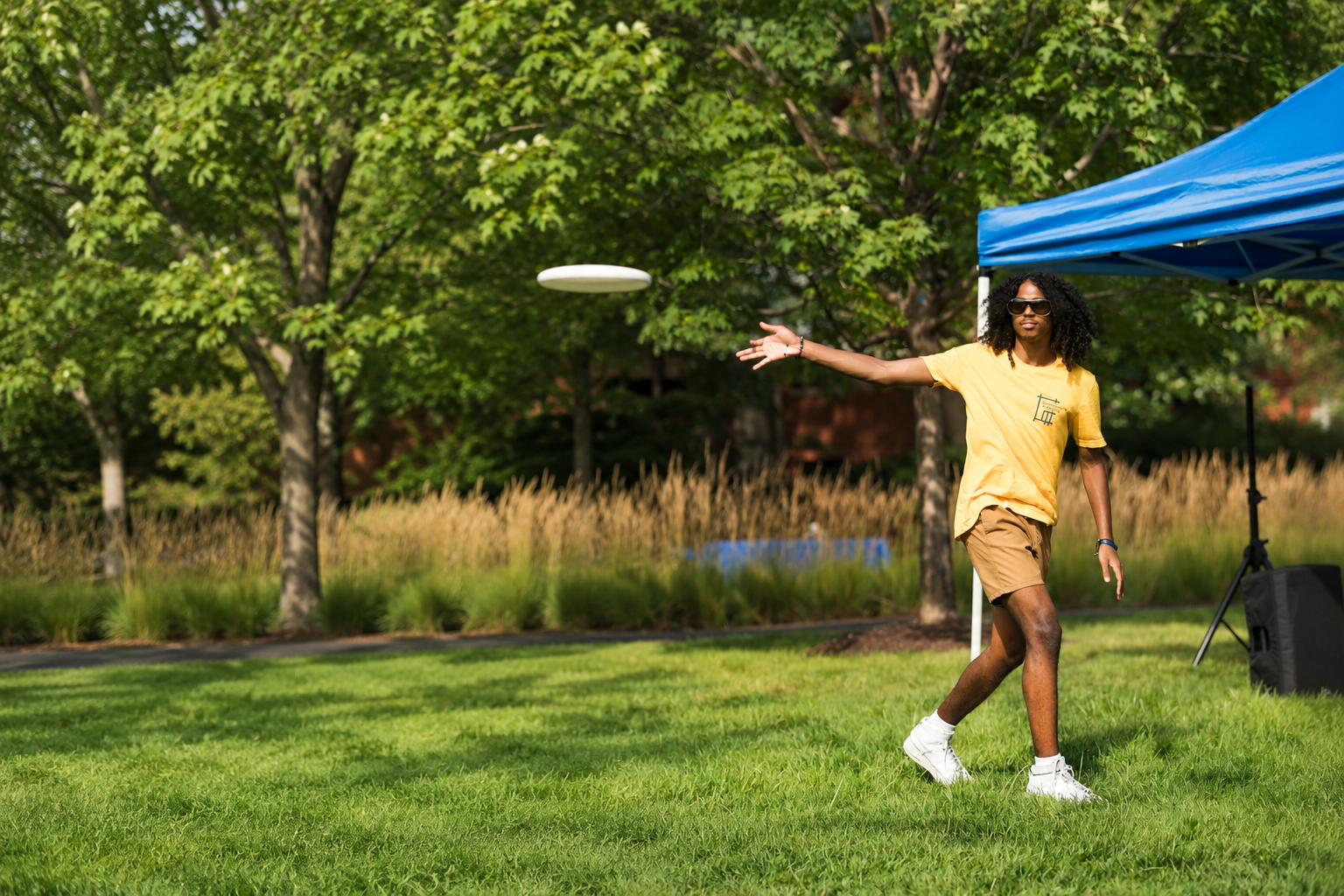 Man in a yellow shirt throwing a frisbee on a lawn next to a cabana
